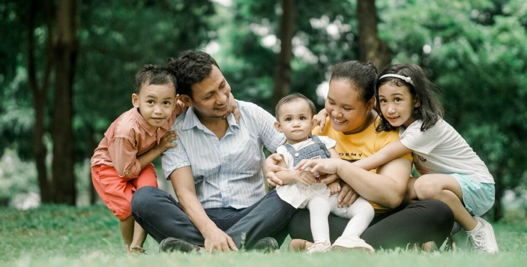 Two parents with their three young children sitting on the grass