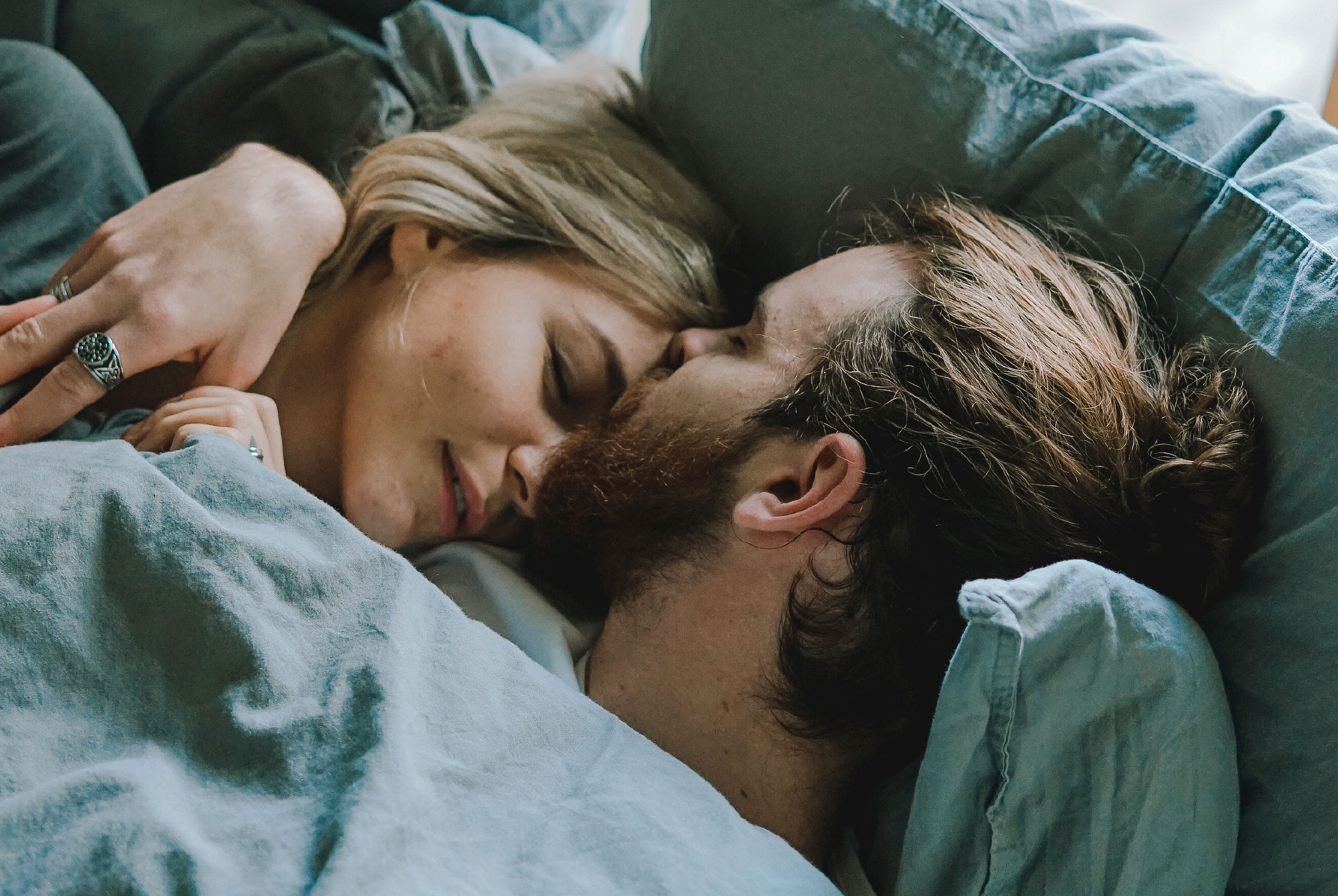 Man and woman lying in bed man with his bad around woman and resting his head against hers