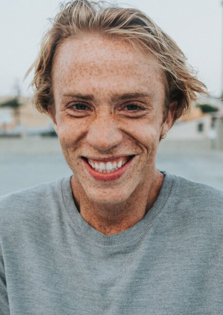 Young man with freckles grinning.