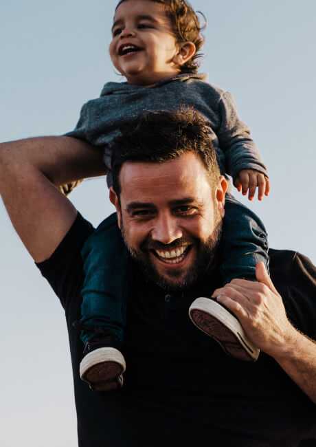 Man with boy toddler on his shoulders laughing.