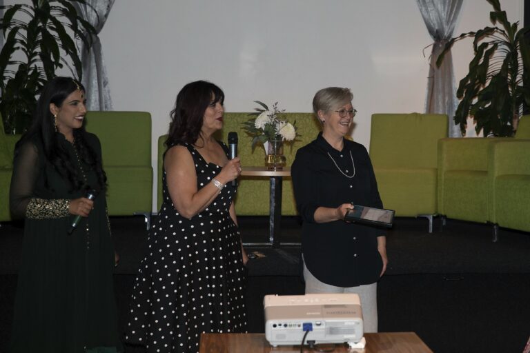 Three women standing up and smiling at an event.