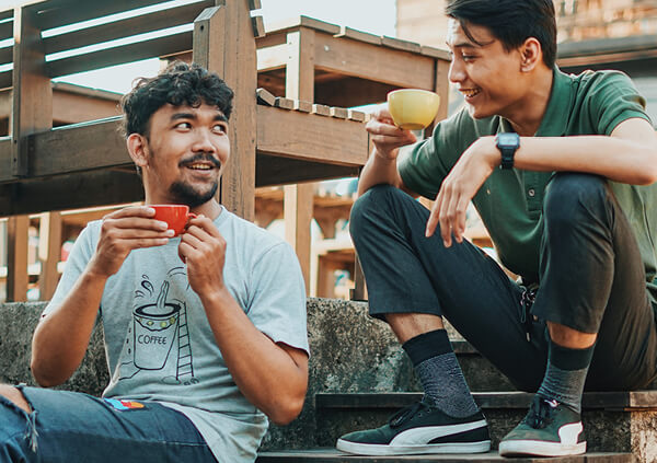 Two men seated on stairs enjoying a cup of tea together.