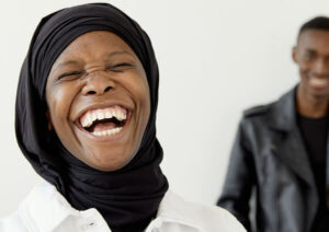 Laughing woman with blurred smiling man in background.