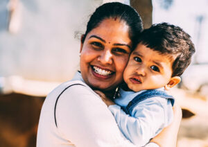 Smiling woman holds a young boy, looking to camera with out of focus background.