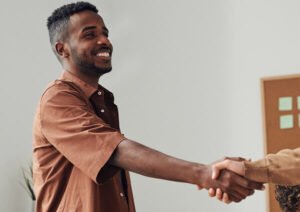 Man in an office environment extends handshake with out of shot colleague.