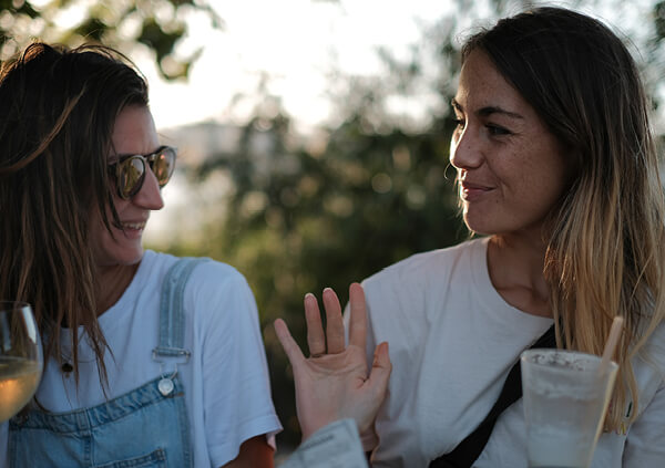 Two female friends outdoors, looking at each other and interacting.