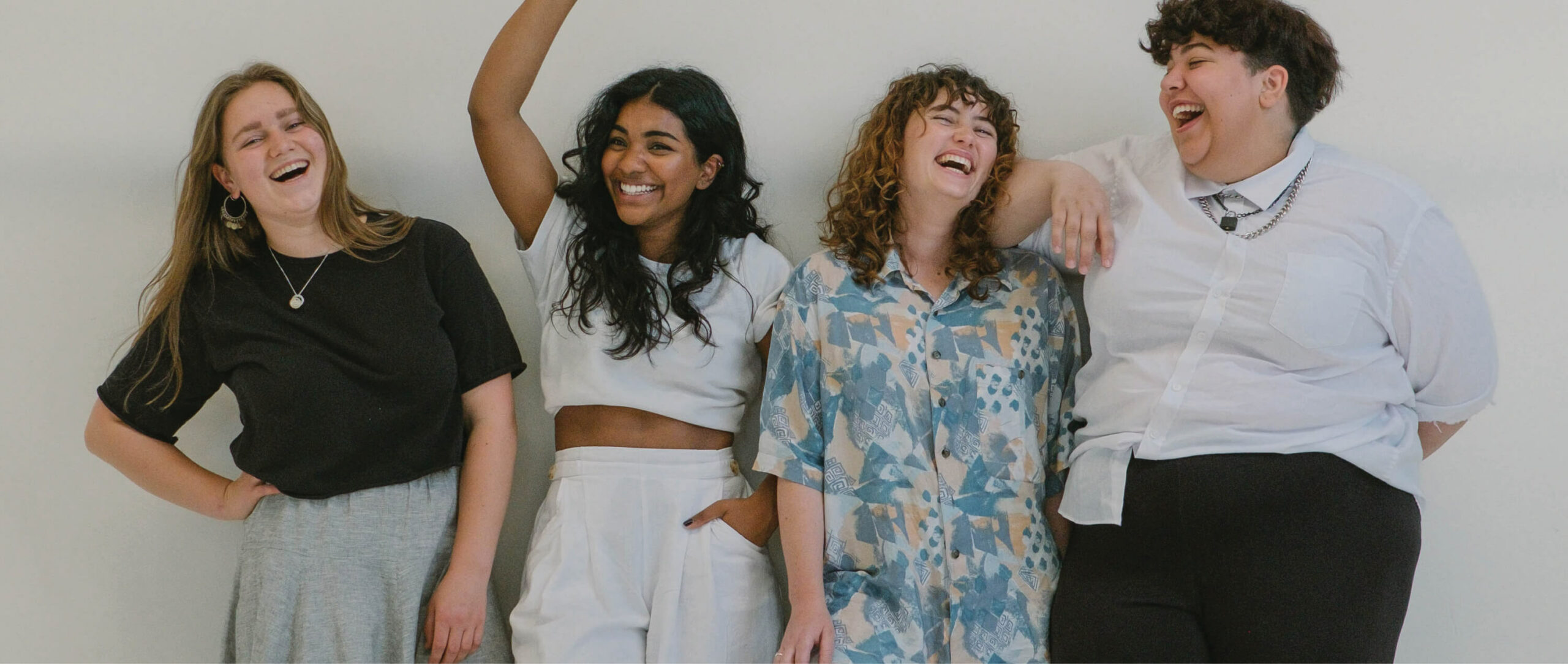 Four women standing against a wall looking happy.