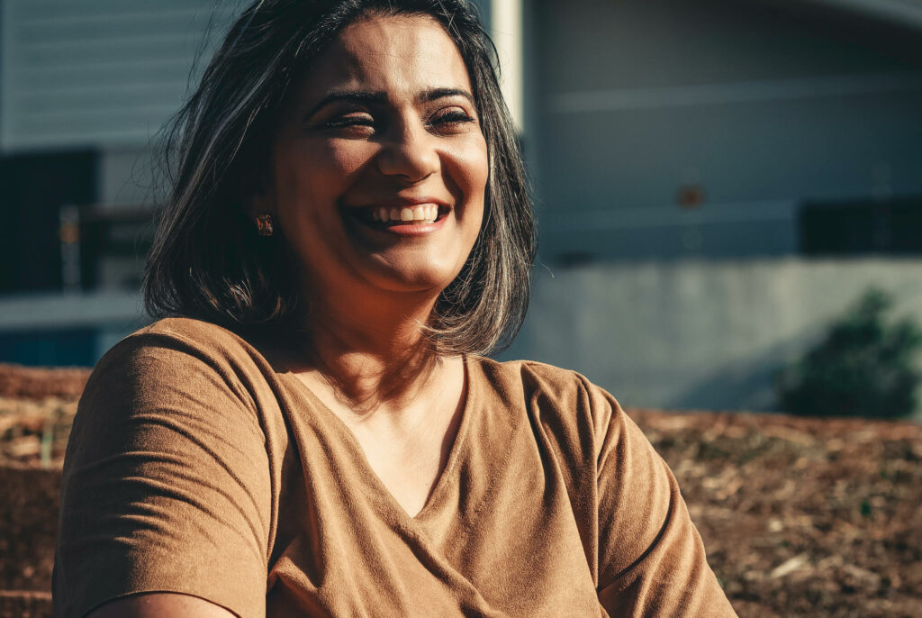 Smiling woman in tan coloured top looking away from camera.