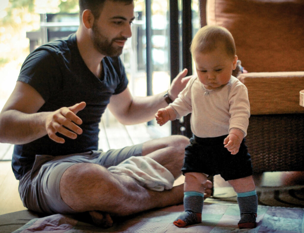 Man sitting on floor with baby learning to walk.