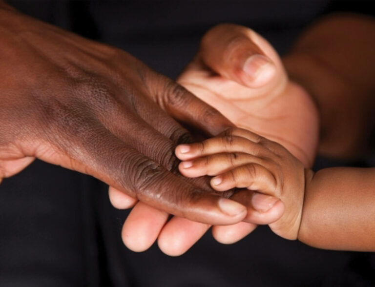 A cropped image of a childs hand holding two adult hands.