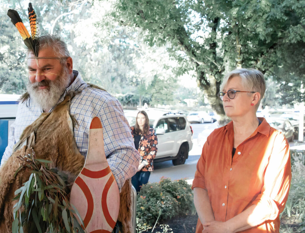 Man in traditional dress next to woman in orange shirt, looking away from camera.