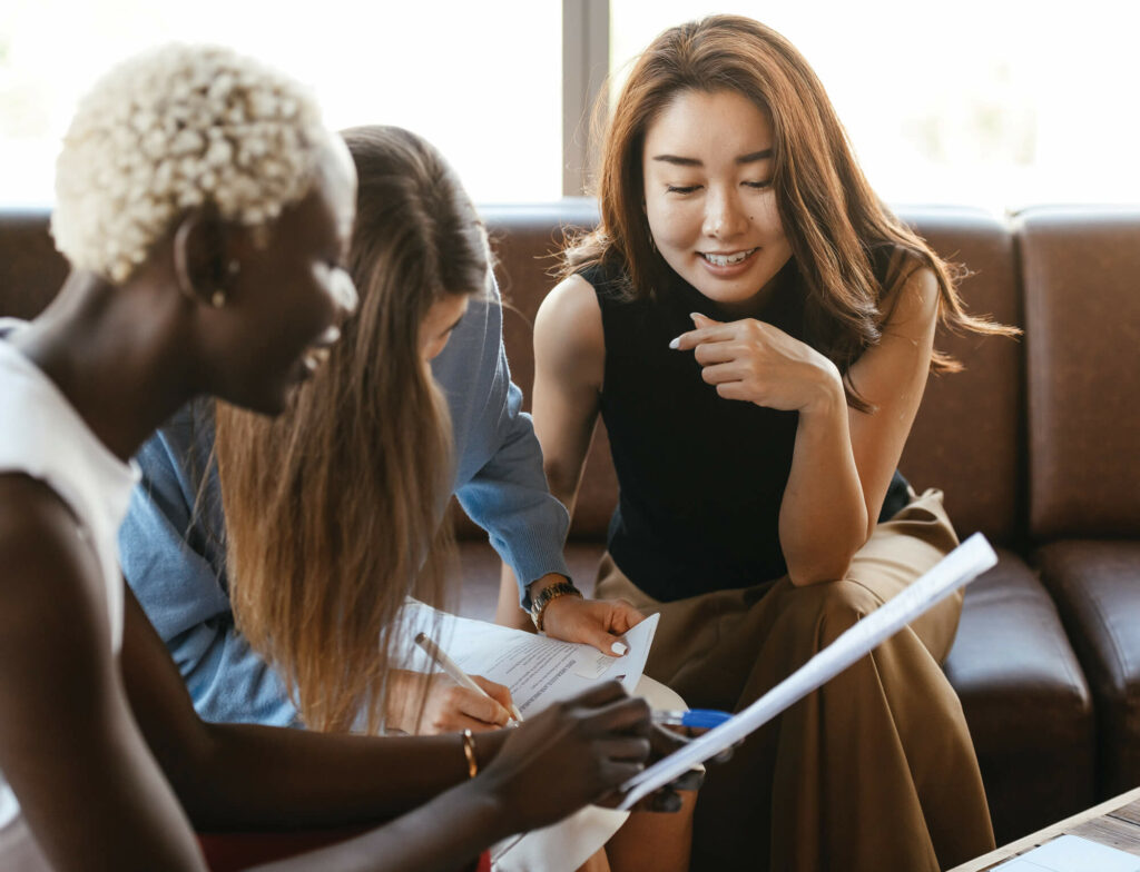 Three women meeting together talking with notes.