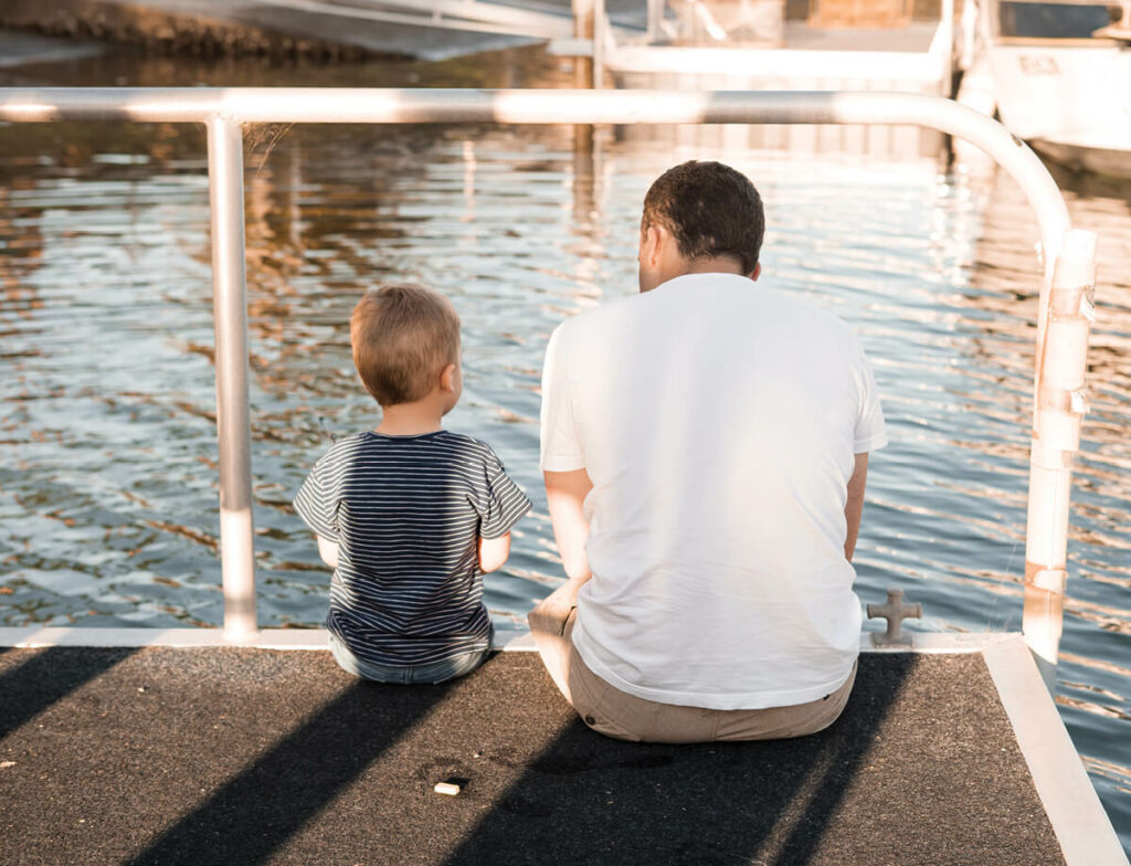 Man sitting on jetty with toddler son.
