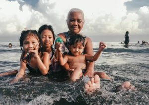 Grandmother with grandchildren sitting in shallow ocean water.