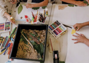 Children surrounding table setting with colouring in and natural materials.