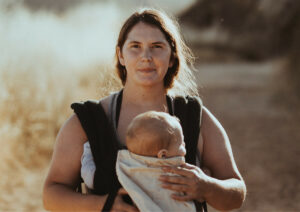 Mother carrying baby in front harness.