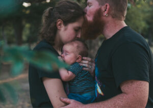 Man kissing forehead of woman holding baby.