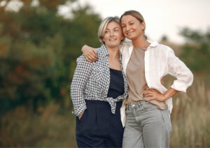 Daughter with arm around mum standing in a grassy field.