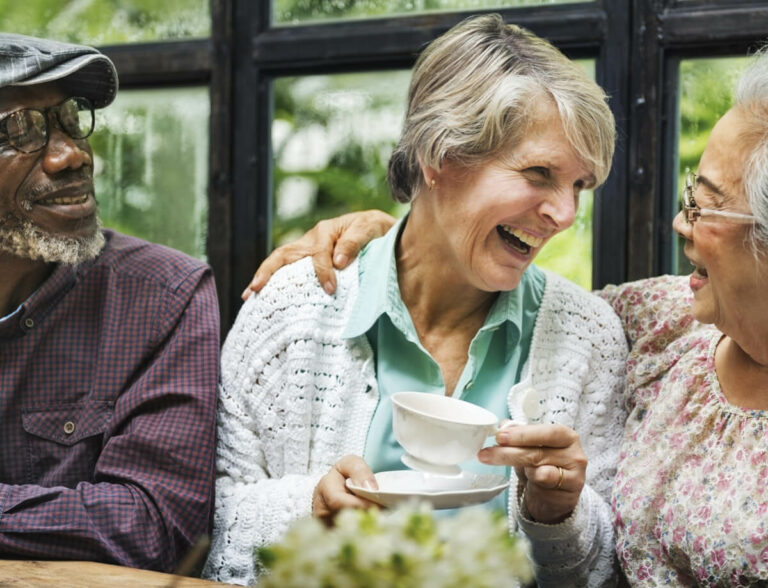 Three elderly people drinking tea laughing together.