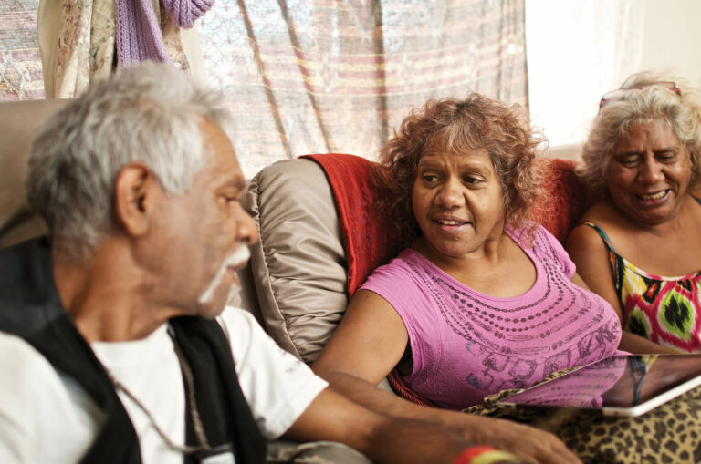 Three elderly indigenous Australians talking together smiling.