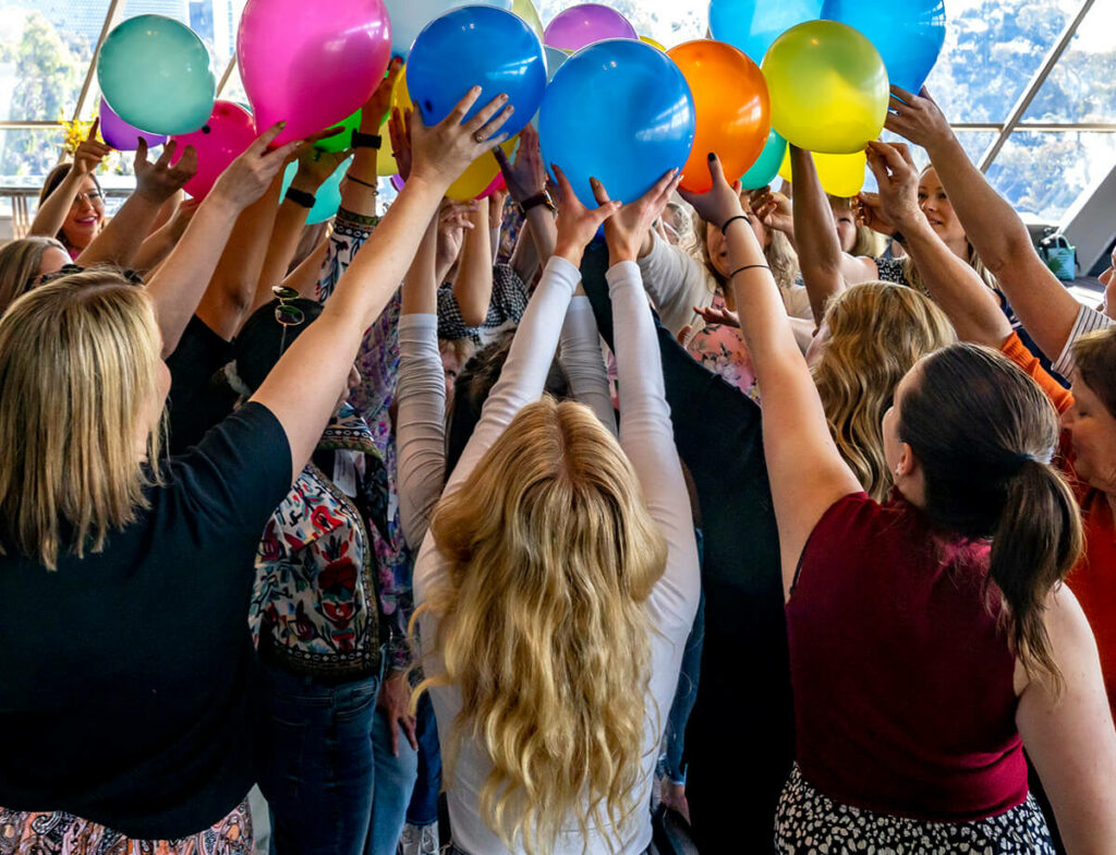 Group of people holding balloons up to touch in the centre.